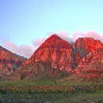 Sléibhte dearga Red Rock Canyon faoi sholas te, le scamaill agus spéir ghorm os a gcionn.